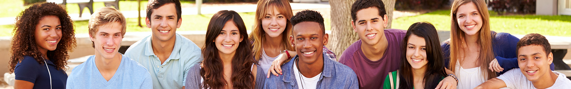 A large group of diverse students sitting on a stone wall around a campus tree.