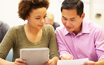 A female student sitting with a male tutor reading from the same piece of paper.