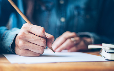 Close up view of two hands, one of them holding a pencil writing on a paper.